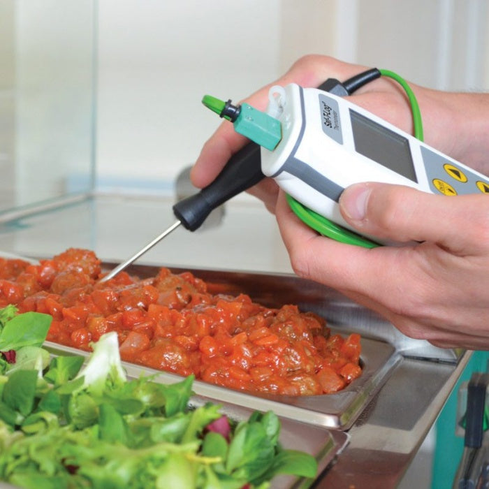 Une personne utilise un Enregistreur Saf-T-Log® HACCP de Thermomètre.fr pour vérifier la température d'un aliment cuit dans une barquette à côté d'une salade, garantissant ainsi le respect des rapports HACCP.
